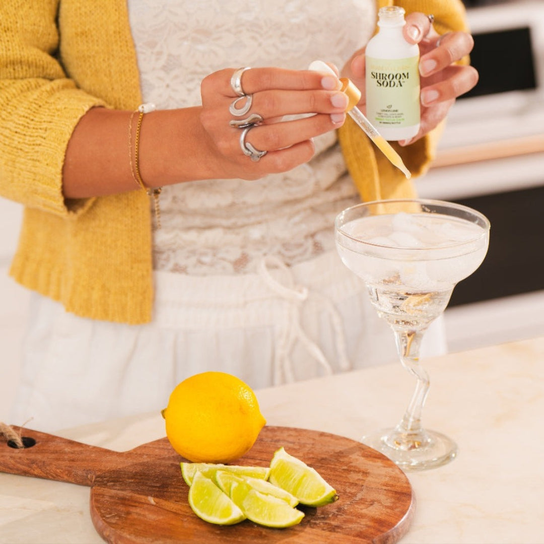 Person pouring a drink into a martini glass with a lemon and lime on a cutting board.