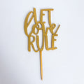 Gold cake topper with 'Let Love Rule' text on a white background