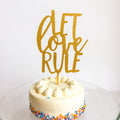 White cake with colorful sprinkles and a gold 'Let Love Rule' topper on a white background