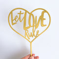 Gold heart-shaped sign with 'Let Love Rule' text on a white background