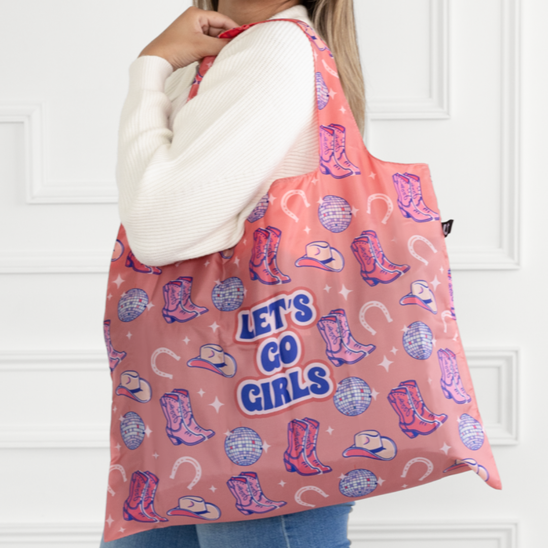 Woman holding a pink tote bag with cowboy boot and hat designs, and 'Let's Go Girls' text.