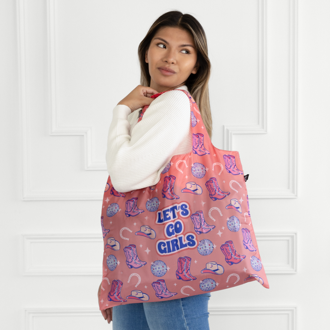 Person holding a pink tote bag with cowboy boot and hat pattern and 'Let's Go Girls' text.