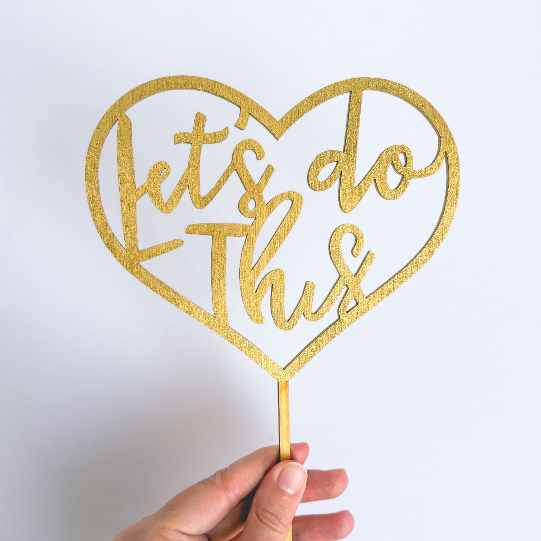 Gold heart-shaped sign with 'Let's do this' text on a white background