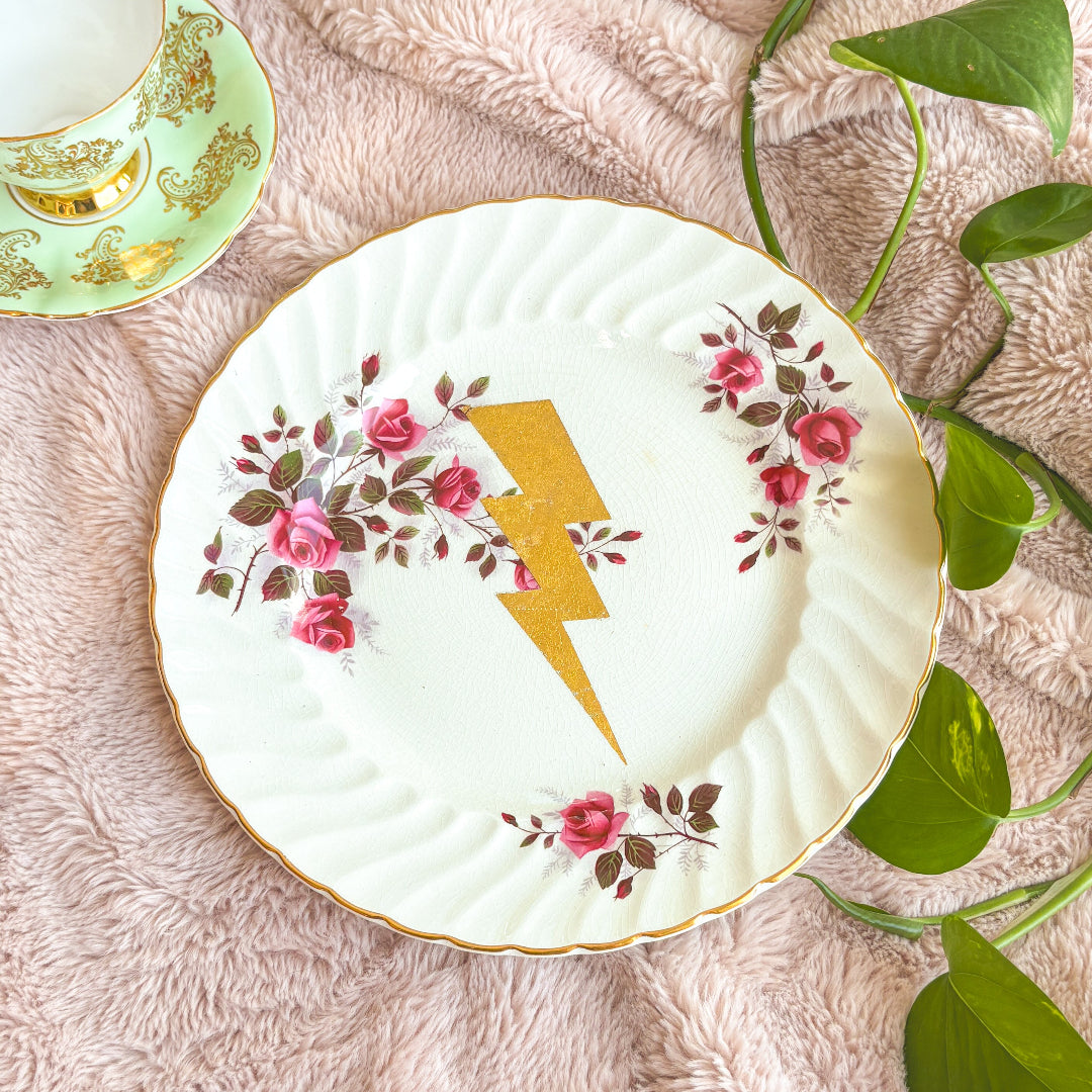Decorative plate with floral design and yellow lightning bolt on a textured surface with leaves.