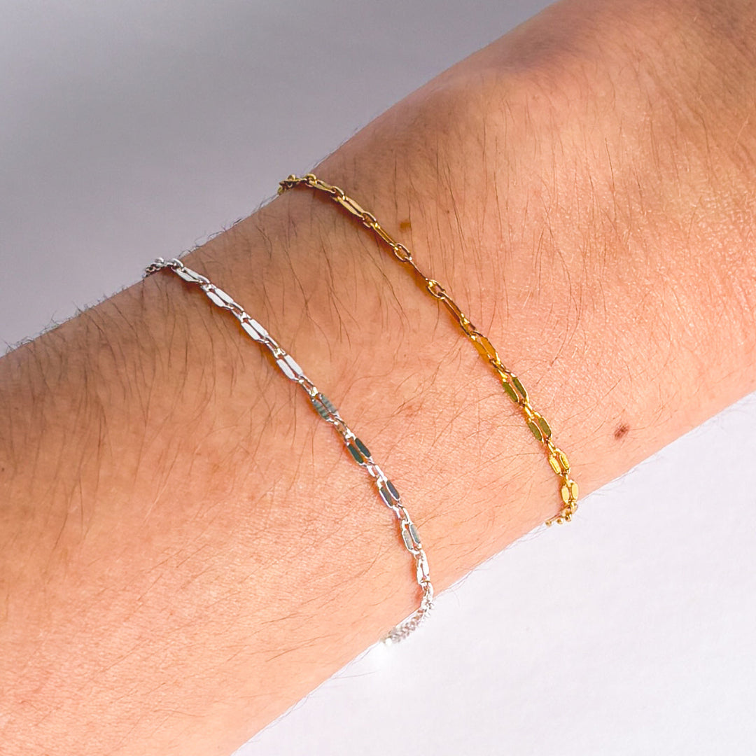 Two bracelets, one gold and one silver, on a wrist against a neutral background.