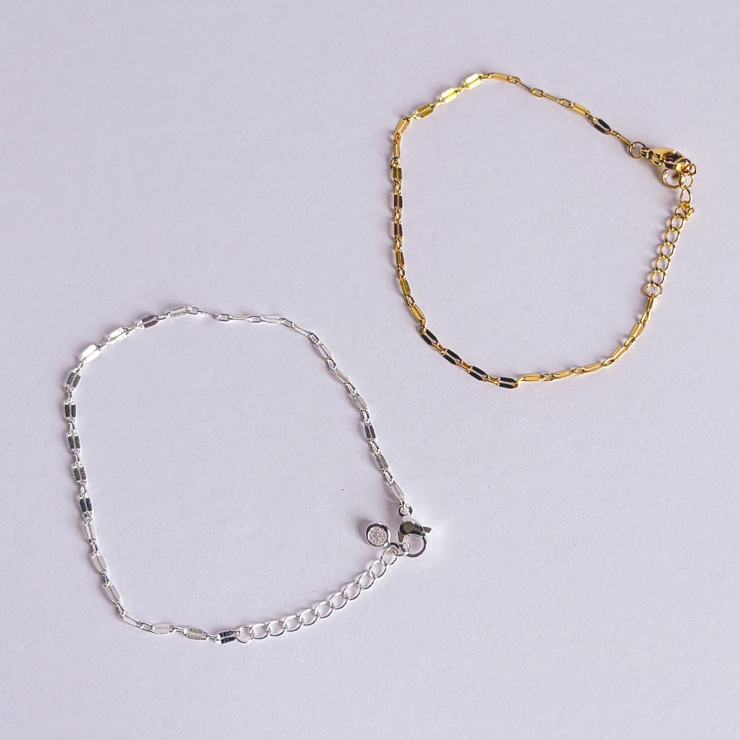 Gold and silver anklets on a light gray background