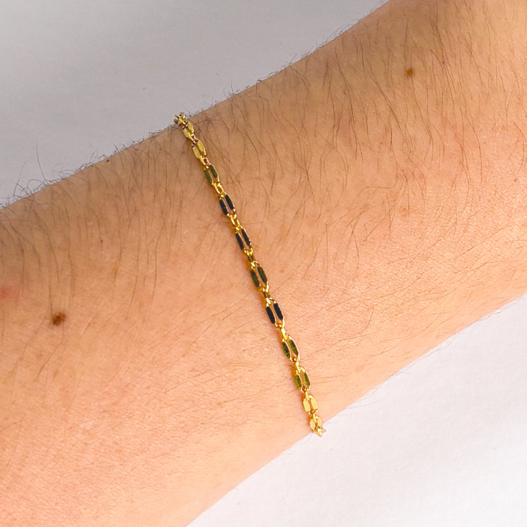 Gold chain bracelet on a wrist with a neutral background