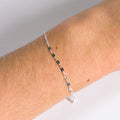 Silver bracelet with green beads on a wrist against a neutral background