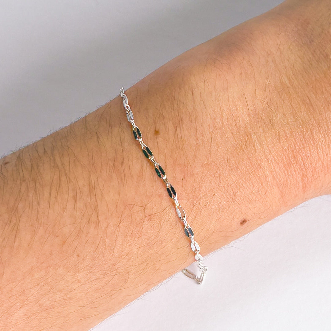 Silver bracelet with green beads on a wrist against a neutral background