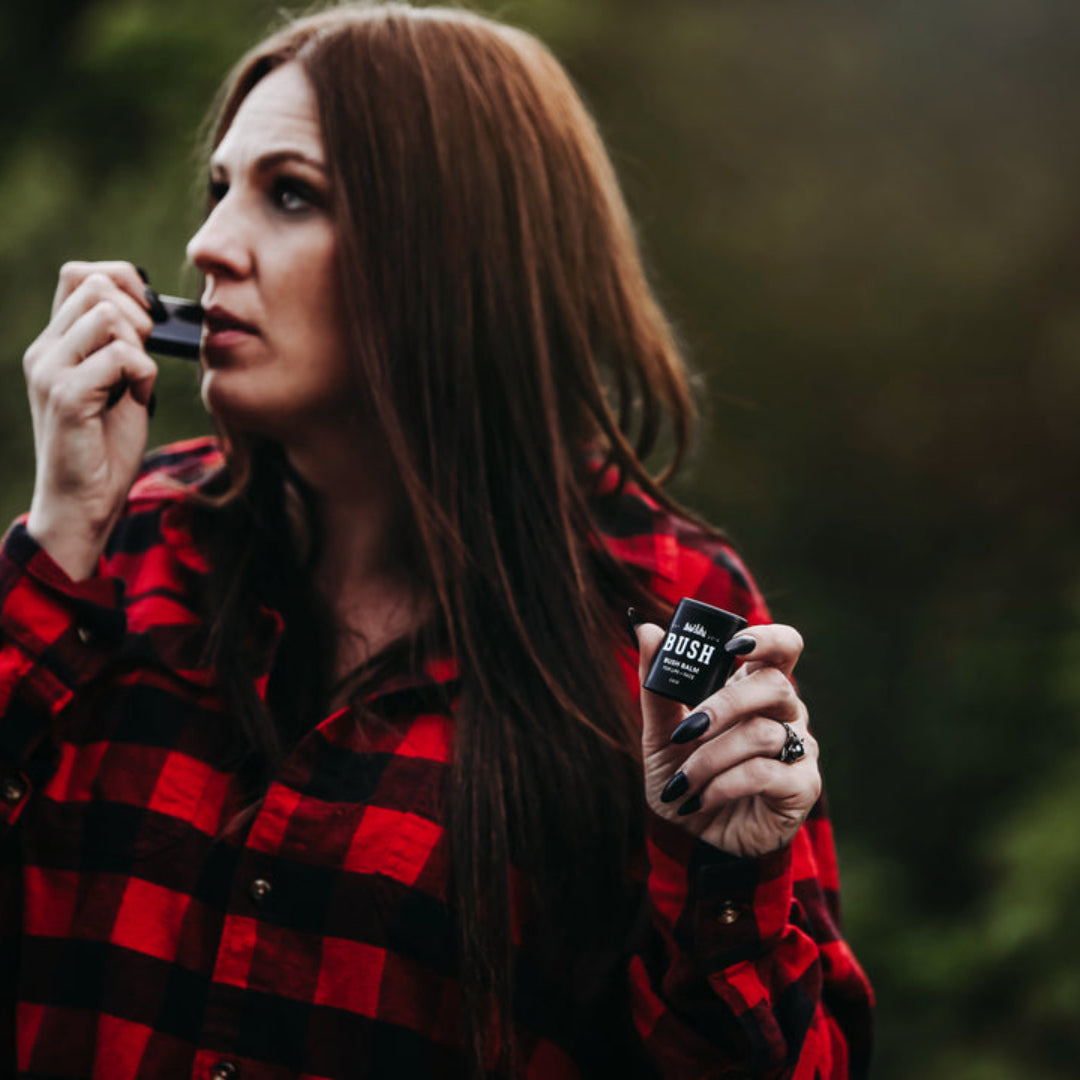 Woman in a red and black plaid shirt holding two small devices against a blurred natural background