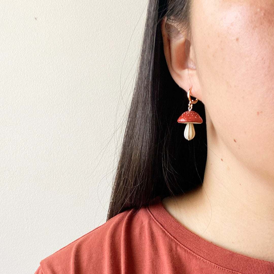 Person wearing a mushroom-shaped earring with a plain background