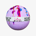A spherical lavender bath bomb with colorful paint-splatter and glitter details, wrapped in a white paper band labeled 'Lollipop Bath Bomb Shop' and 'Bath Bomb'.
