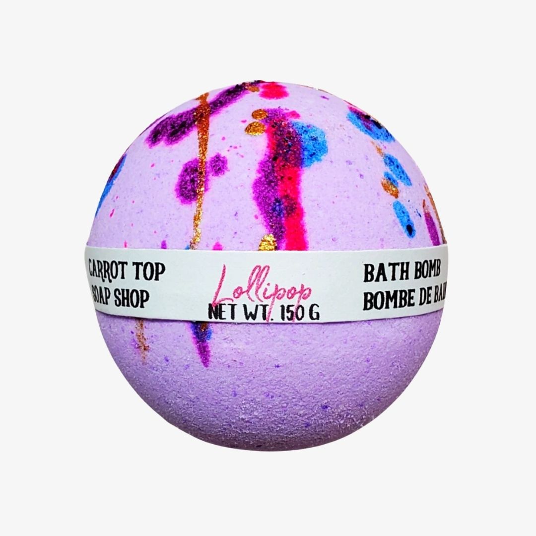 A spherical lavender bath bomb with colorful paint-splatter and glitter details, wrapped in a white paper band labeled 'Lollipop Bath Bomb Shop' and 'Bath Bomb'.