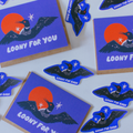 A set of die-cut stickers and a matching square card featuring a stylized loony bird illustration. The design shows a dark blue bird with outstretched wings over a bright orange sun and white stars, with the text 'LOONY FOR BIRDS' on the card and smaller 'LOONY FOR BIRDS' text on the stickers.