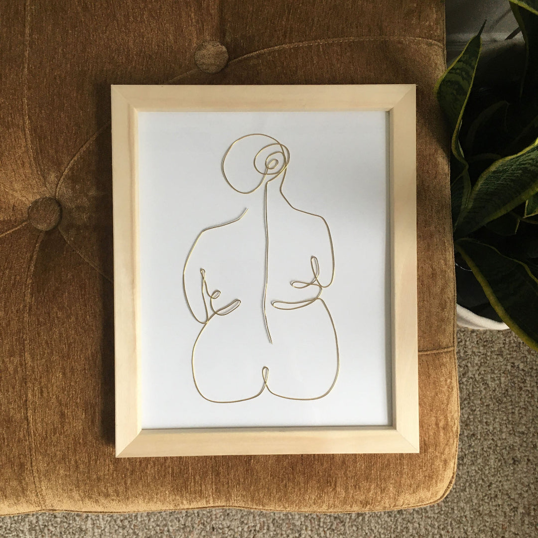 Framed abstract line art of a nude figure on a textured surface