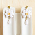 White flower earrings with gold centers on a white stand against a beige background