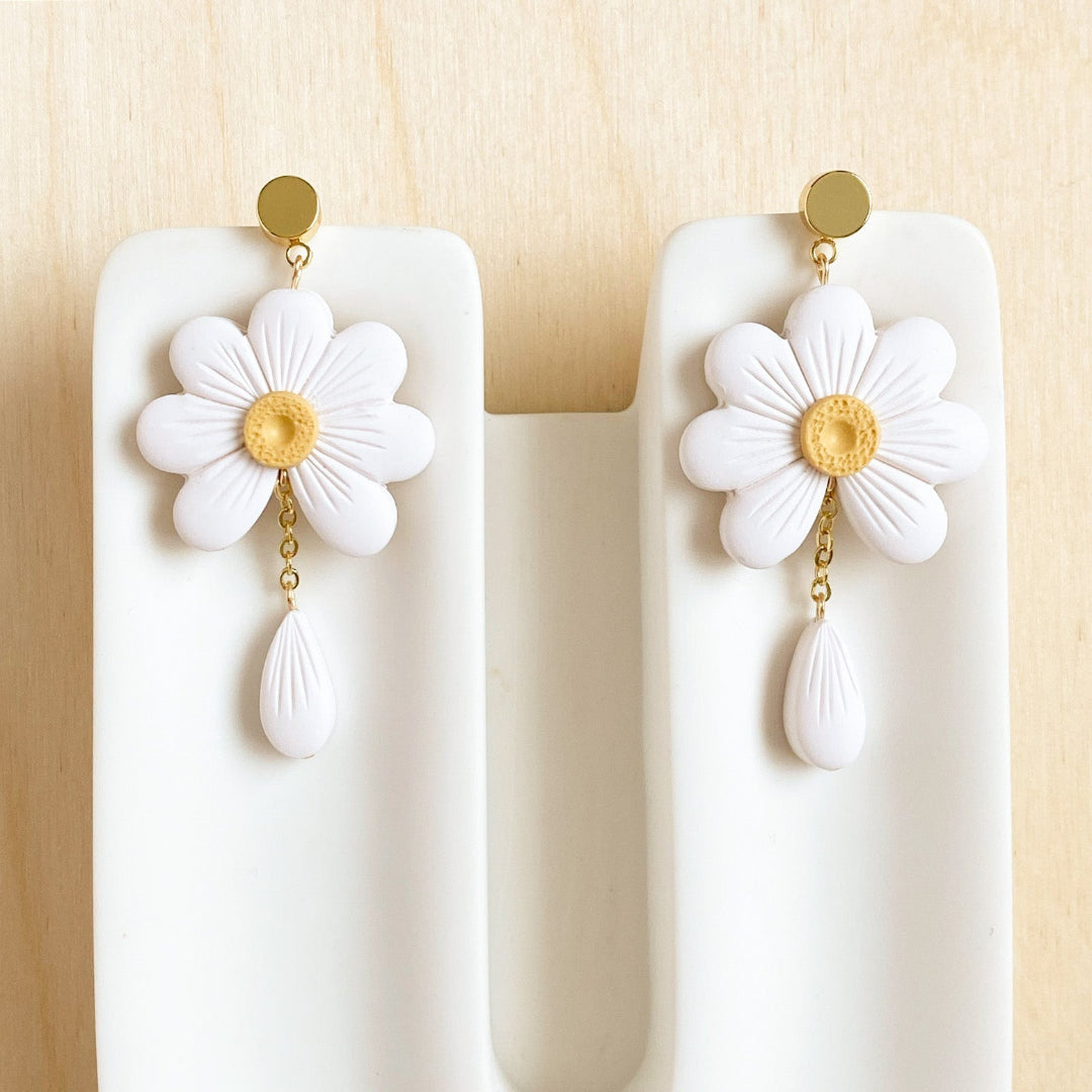 White flower earrings with gold centers on a white stand against a beige background