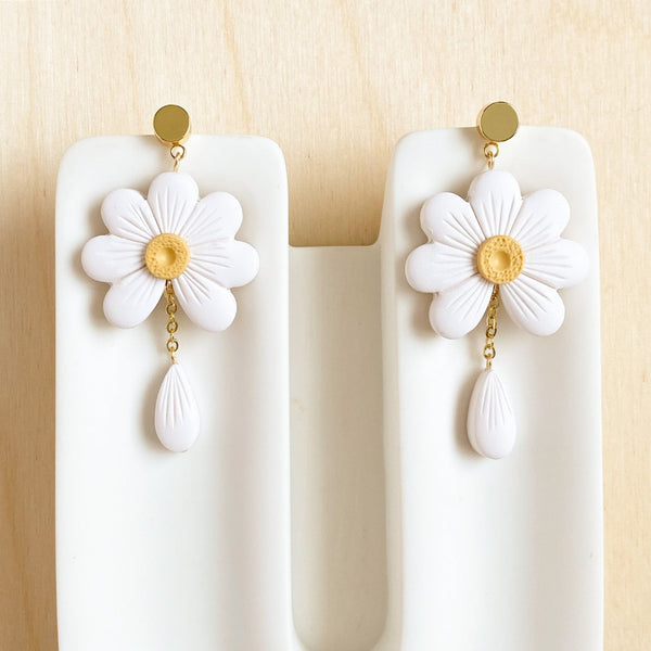 White flower earrings with gold centers on a white stand against a beige background