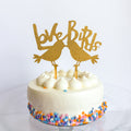 White cake with colorful sprinkles and a gold 'Love Birds' cake topper on a white background