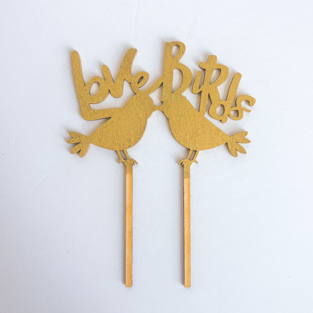 Gold 'Love Birds' cake topper on a white background
