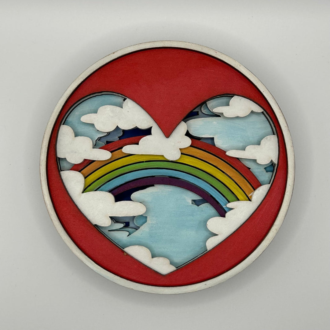 Decorative wall piece with a heart design featuring a rainbow and clouds on a gray background