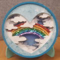 Decorative item with a rainbow and clouds on a stand against a neutral background