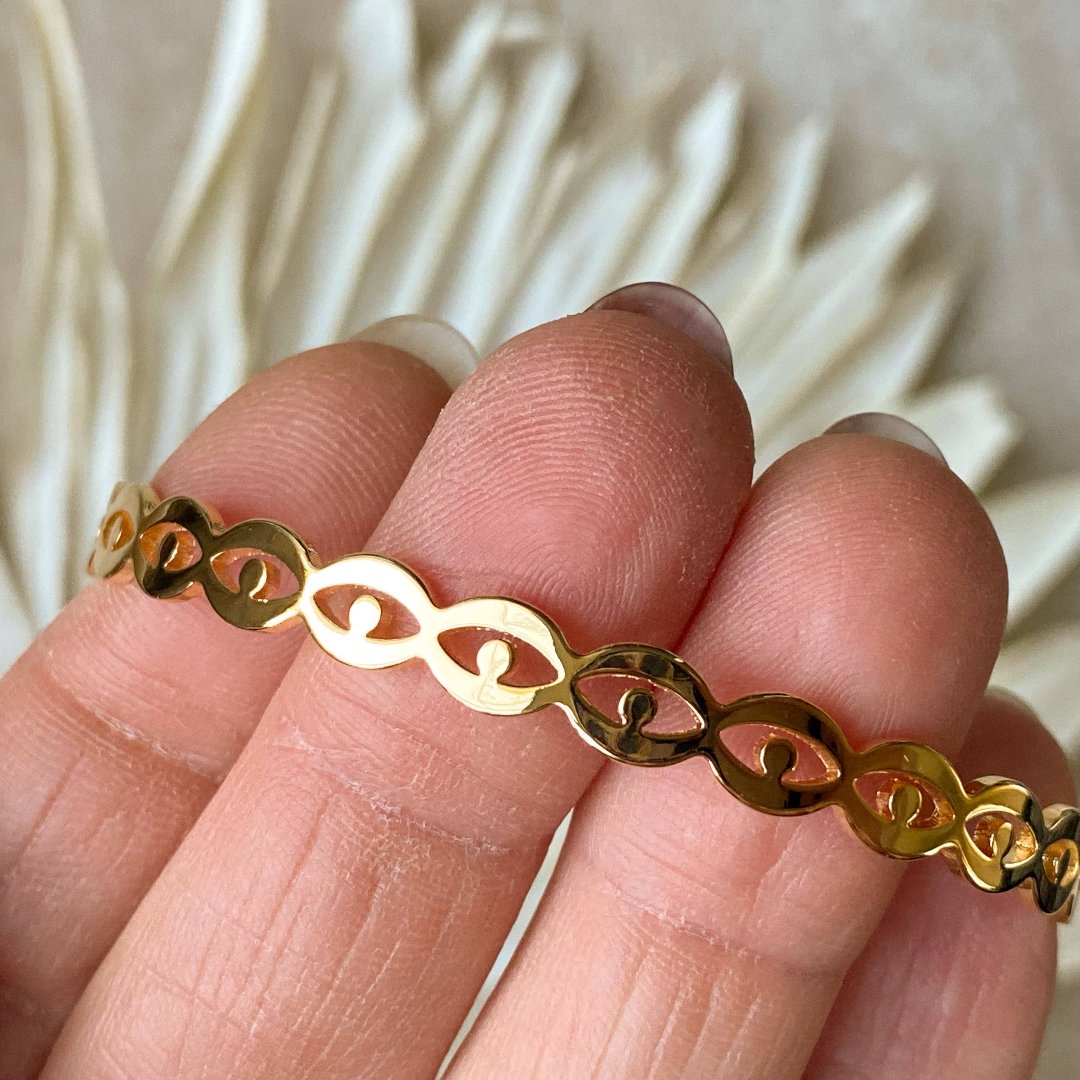 A gold-toned cuff bracelet with a pattern of repeating eye shapes.