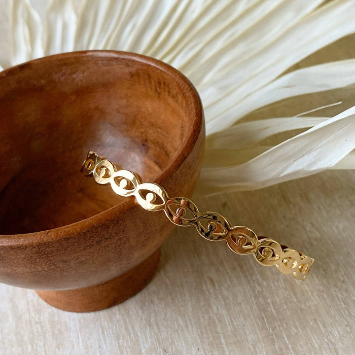 A gold-toned cuff bracelet with a pattern of repeating eye shapes.