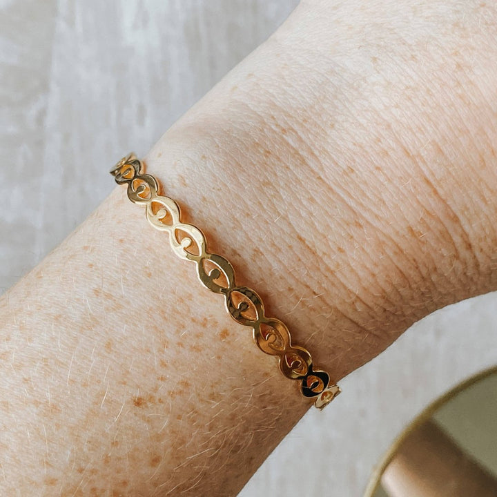 A gold-toned cuff bracelet with a pattern of repeating eye shapes.
