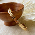 A gold-toned cuff bracelet with a pattern of repeating eye shapes.