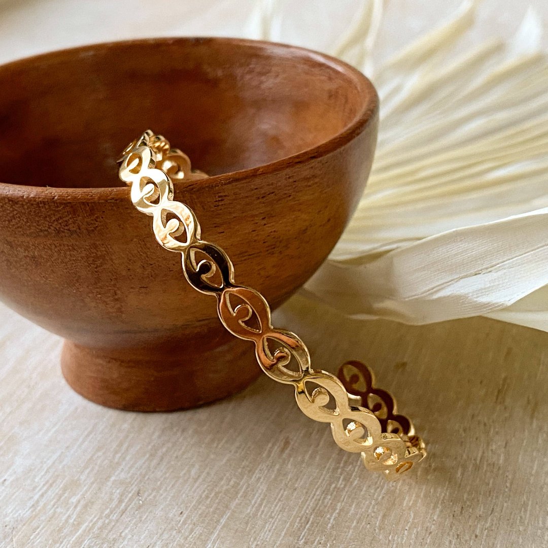 A gold-toned cuff bracelet with a pattern of repeating eye shapes.