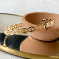 A gold-toned cuff bracelet with a pattern of repeating eye shapes.