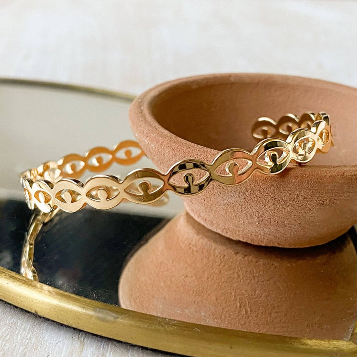 A gold-toned cuff bracelet with a pattern of repeating eye shapes.