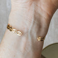 A gold-toned cuff bracelet with a pattern of repeating eye shapes.