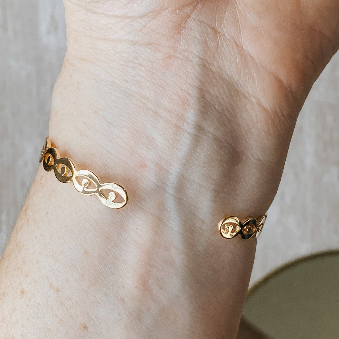 A gold-toned cuff bracelet with a pattern of repeating eye shapes.