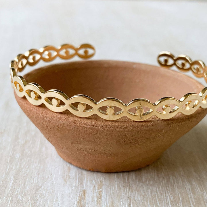 A gold-toned cuff bracelet with a pattern of repeating eye shapes.
