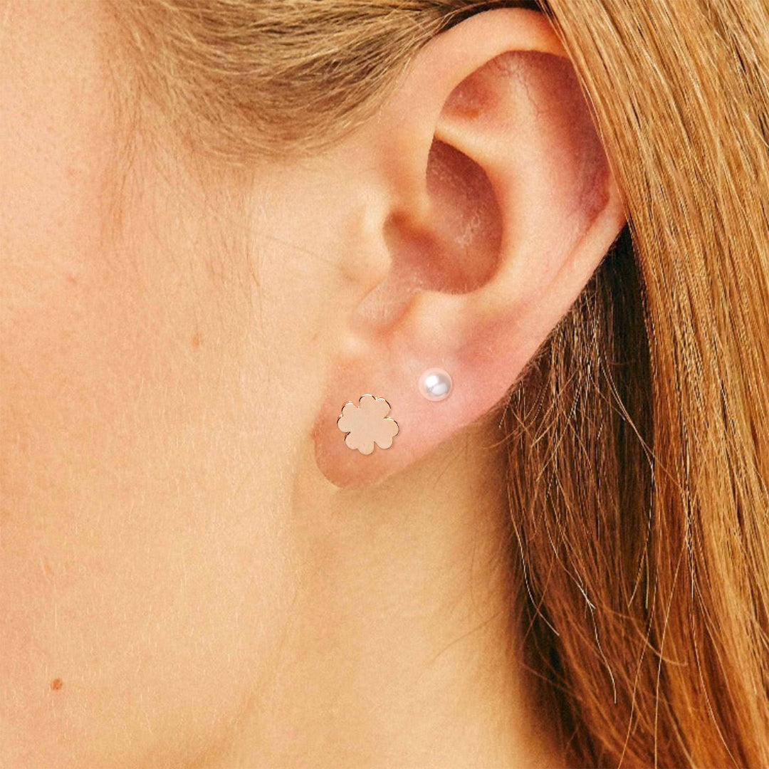 Close-up of an ear wearing a gold flower earring and a pearl stud earring.