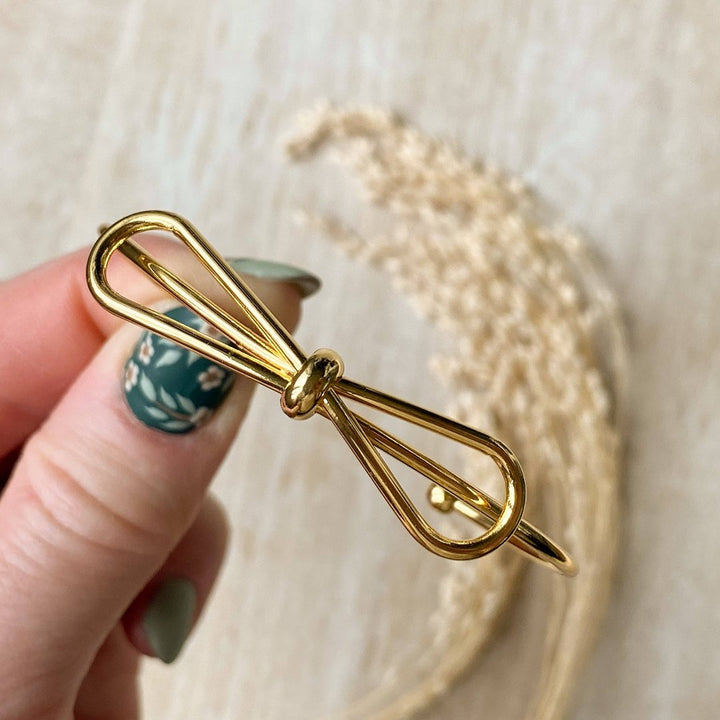 A gold-toned bangle bracelet with a bow design.