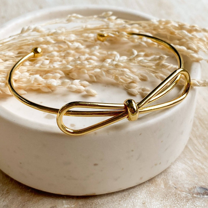 A gold-toned bangle bracelet with a bow design.