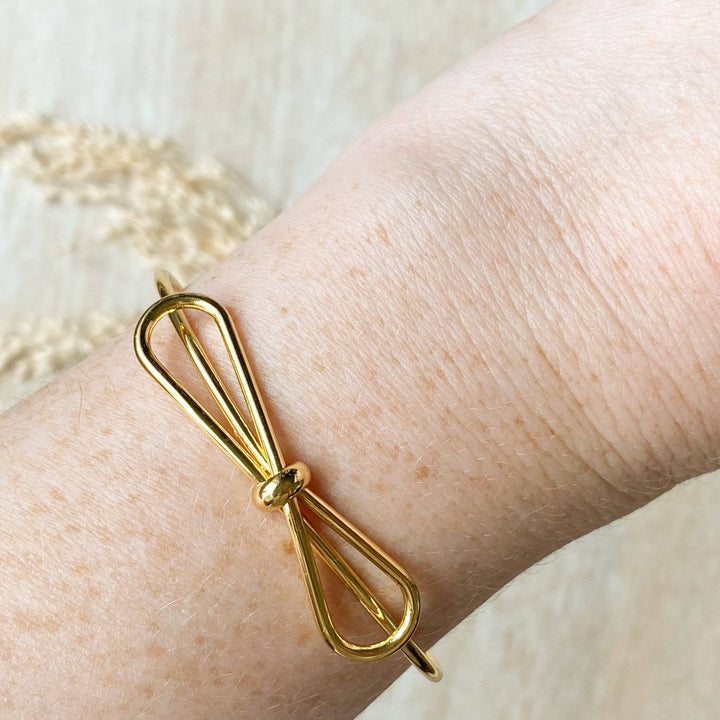 A gold-toned bangle bracelet with a bow design.