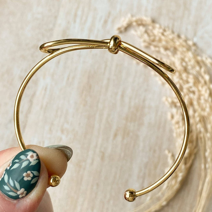 A gold-toned bangle bracelet with a bow design.
