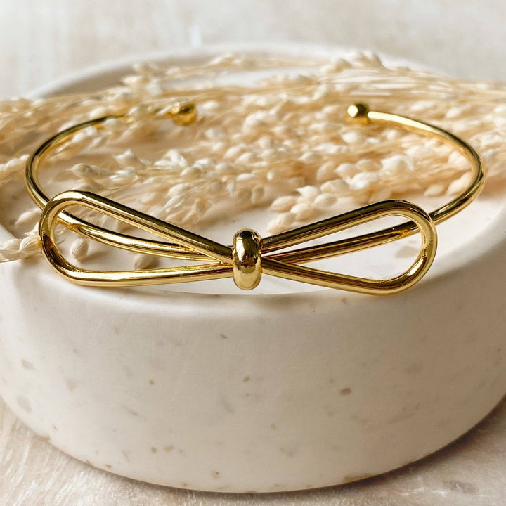 A gold-toned bangle bracelet with a bow design.