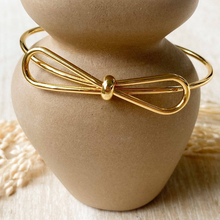 A gold-toned bangle bracelet with a bow design.