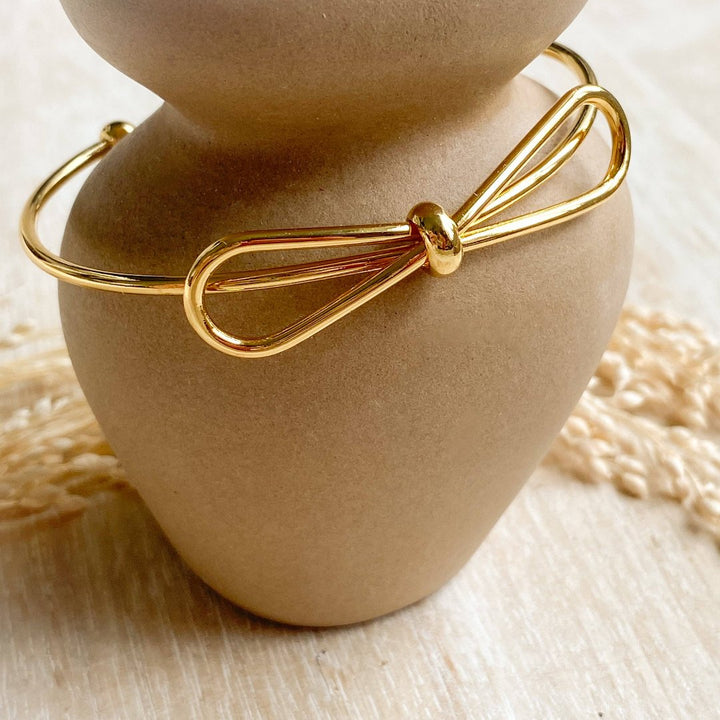 A gold-toned bangle bracelet with a bow design.