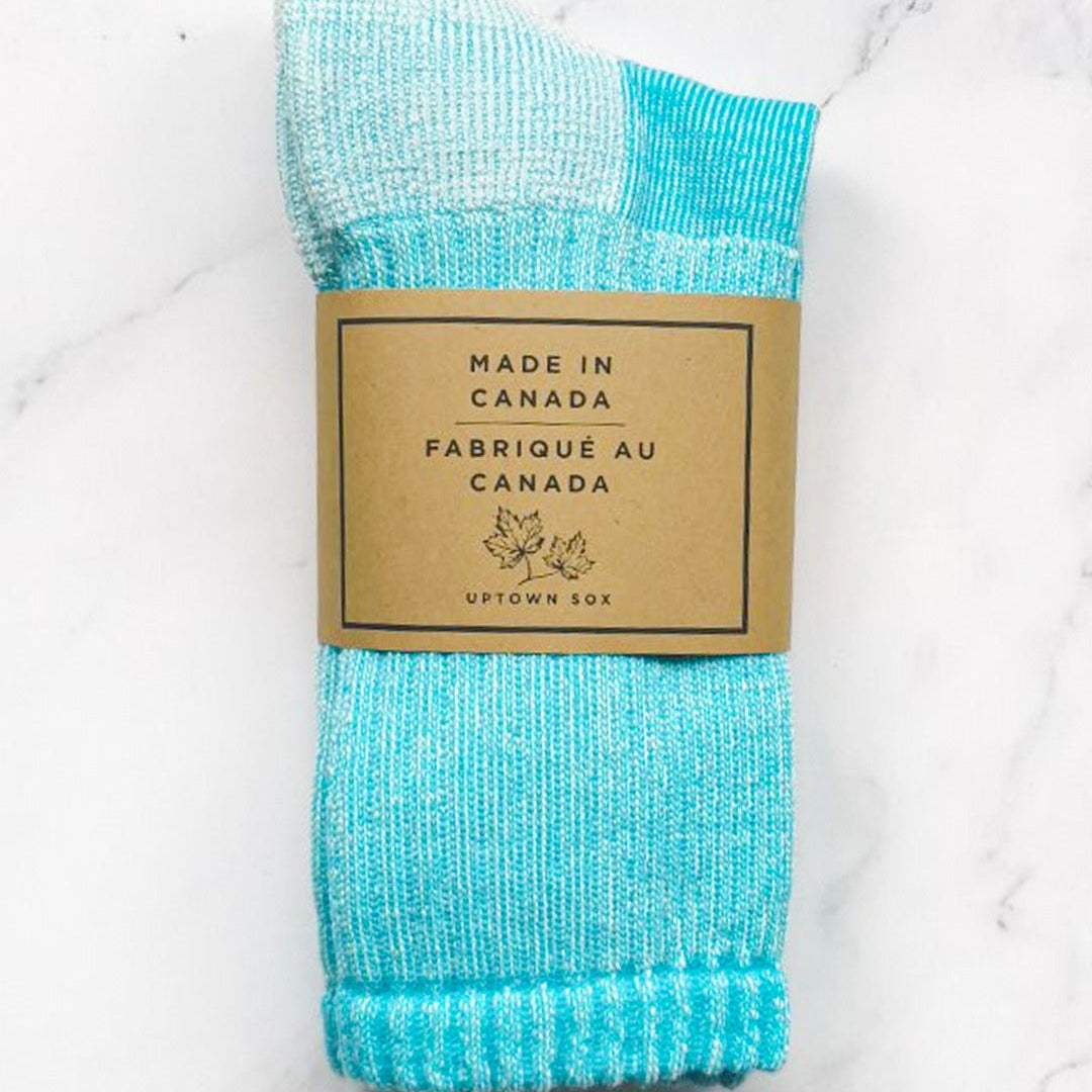 Turquoise sock with a 'Made in Canada' label on a white marble background