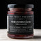 A jar of Maraschino Cherries from Top Shelf Preserves. The jar is filled with red cherries and has a black label with white text. The label includes the product name, 