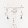 Pair of earrings with gold hooks and white and blue teardrop-shaped stones on a clear stand.