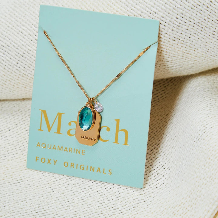 A gold necklace with an aquamarine stone pendant. The pendant also has the word 