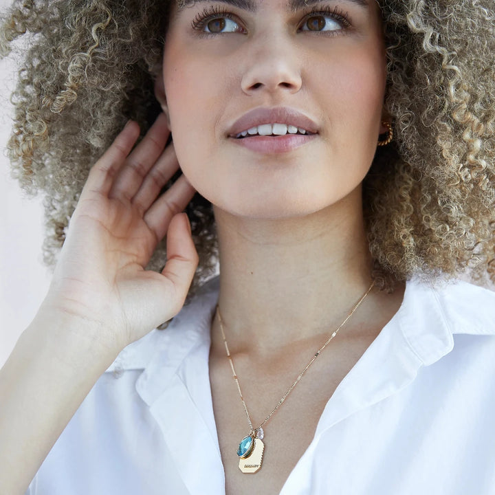 A gold necklace with an aquamarine stone pendant. The pendant also has the word 