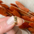Gold ring on a finger with dried orange flowers in the background